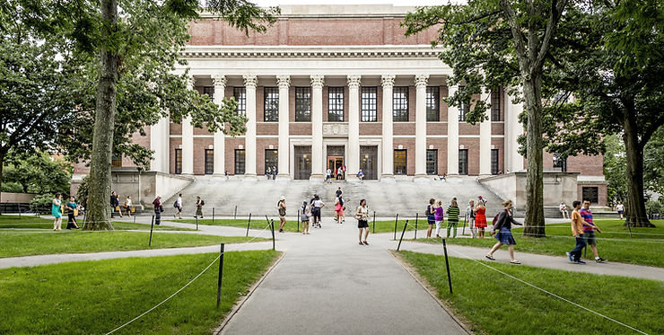 People walk on paths through a green campus with trees. A large brick and column building in the background, creating a vibrant, scholarly scene.